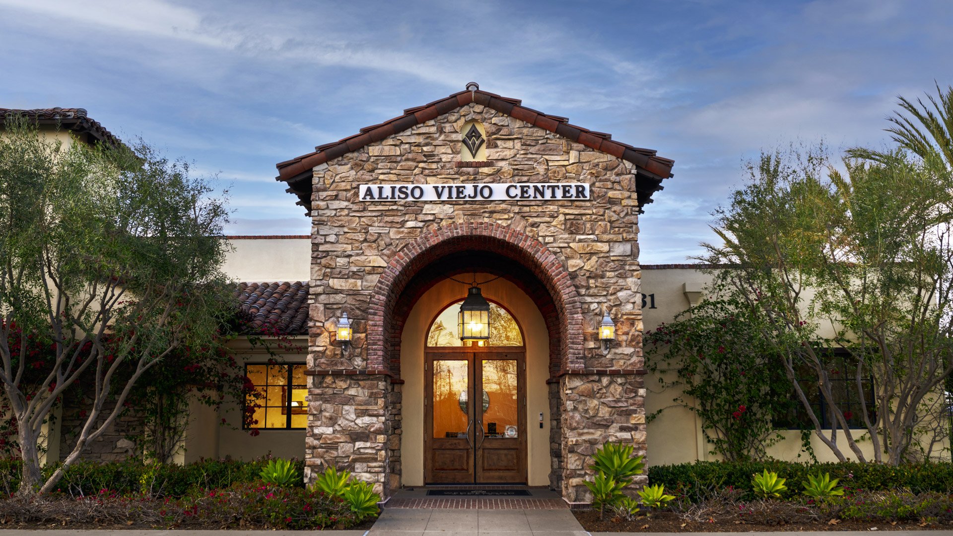 Illuminated stone entrance gate with 'Aliso Viejo Center' signage, arched doorway, and landscaping at Wedgewood Weddings venue in California