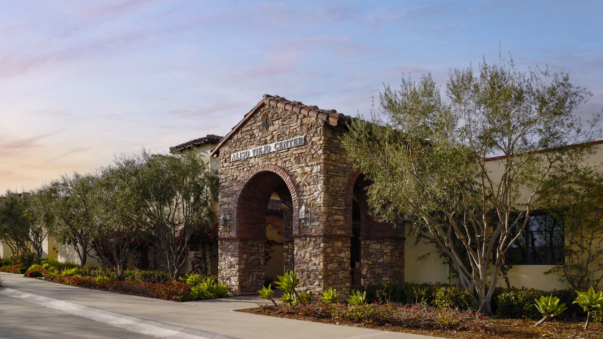 Stone entrance gate with 'Aliso Viejo Center' signage surrounded by landscaped gardens at Wedgewood Weddings venue in Aliso Viejo, California