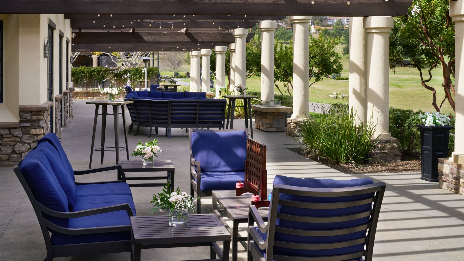 Sophisticated covered patio with navy blue seating, string lights, stone columns, and panoramic golf course views at Aliso Viejo by Wedgewood Weddings