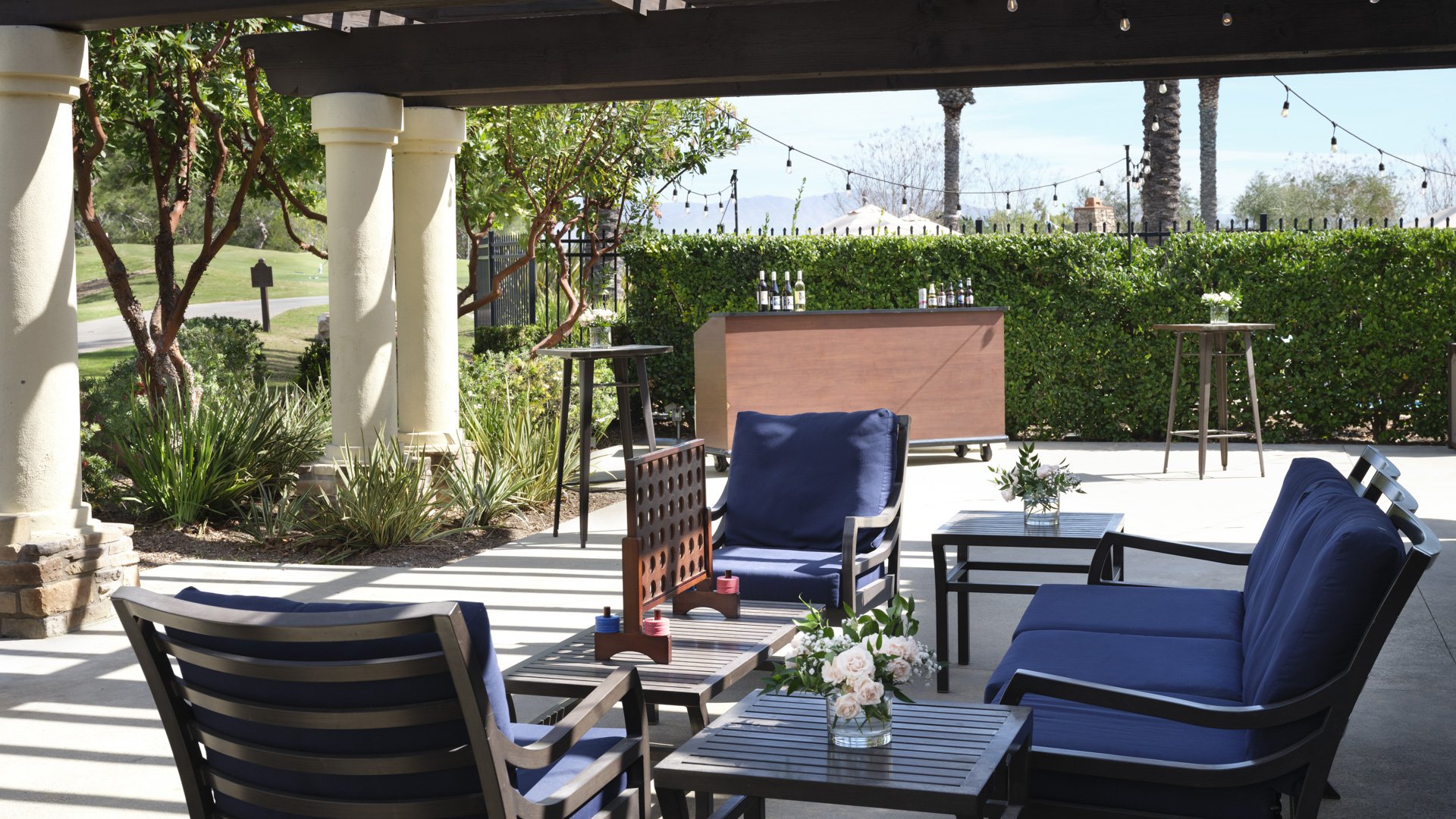 Elegant covered patio with navy cushioned seating, string lights, wooden bar, and golf course views at Aliso Viejo by Wedgewood Weddings venue