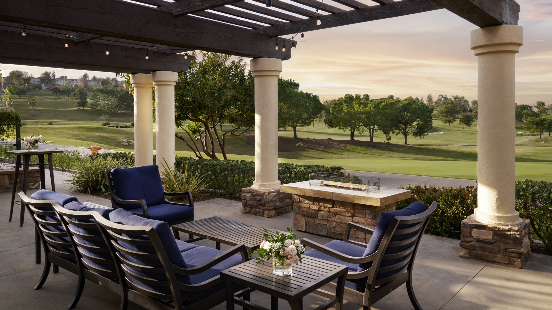 Luxurious covered patio with navy blue cushioned seating, stone fireplace, and panoramic golf course views at Aliso Viejo by Wedgewood Weddings California venue