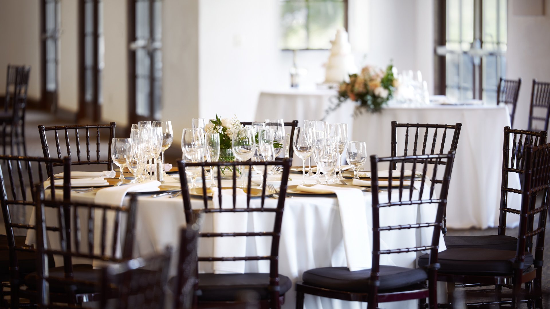 Sophisticated indoor wedding reception table with multiple wine glasses, gold chargers, black Chiavari chairs, and wedding cake display at Aliso Viejo by Wedgewood Weddings California venue