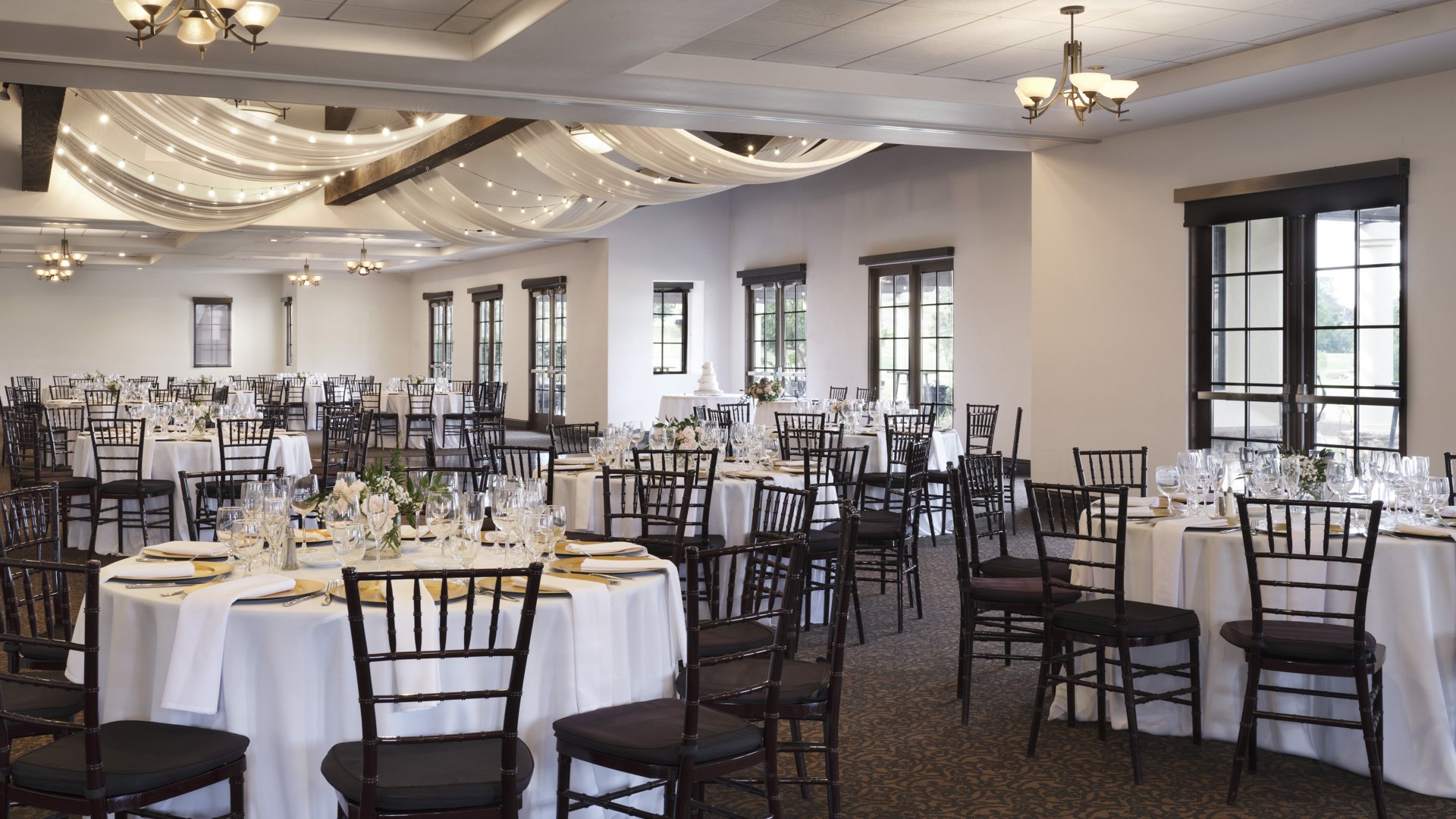 Spacious wedding reception ballroom with elegant ceiling draping, round tables, black chairs, and ambient lighting at Aliso Viejo California venue