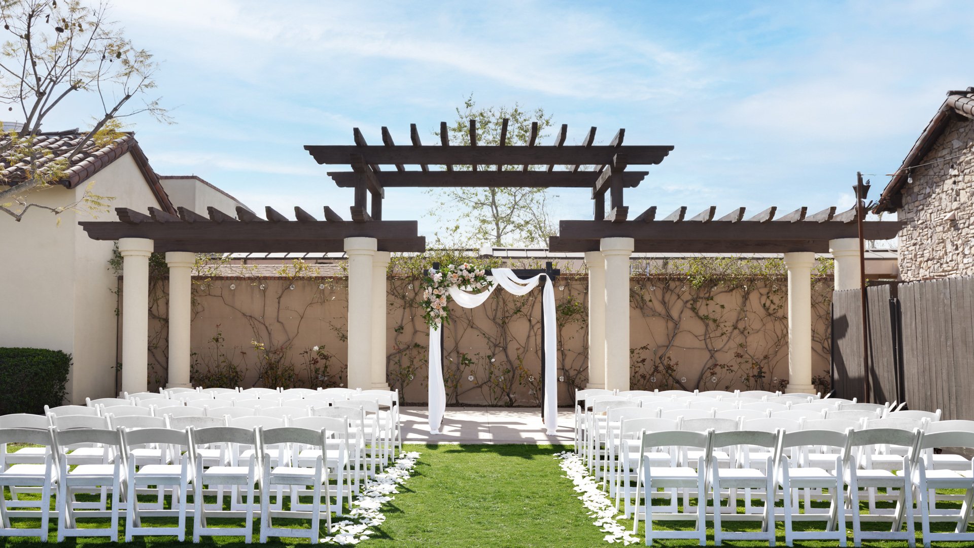 Romantic outdoor wedding ceremony setup with white chairs, floral aisle petals, and wooden pergola altar at Aliso Viejo by Wedgewood Weddings California