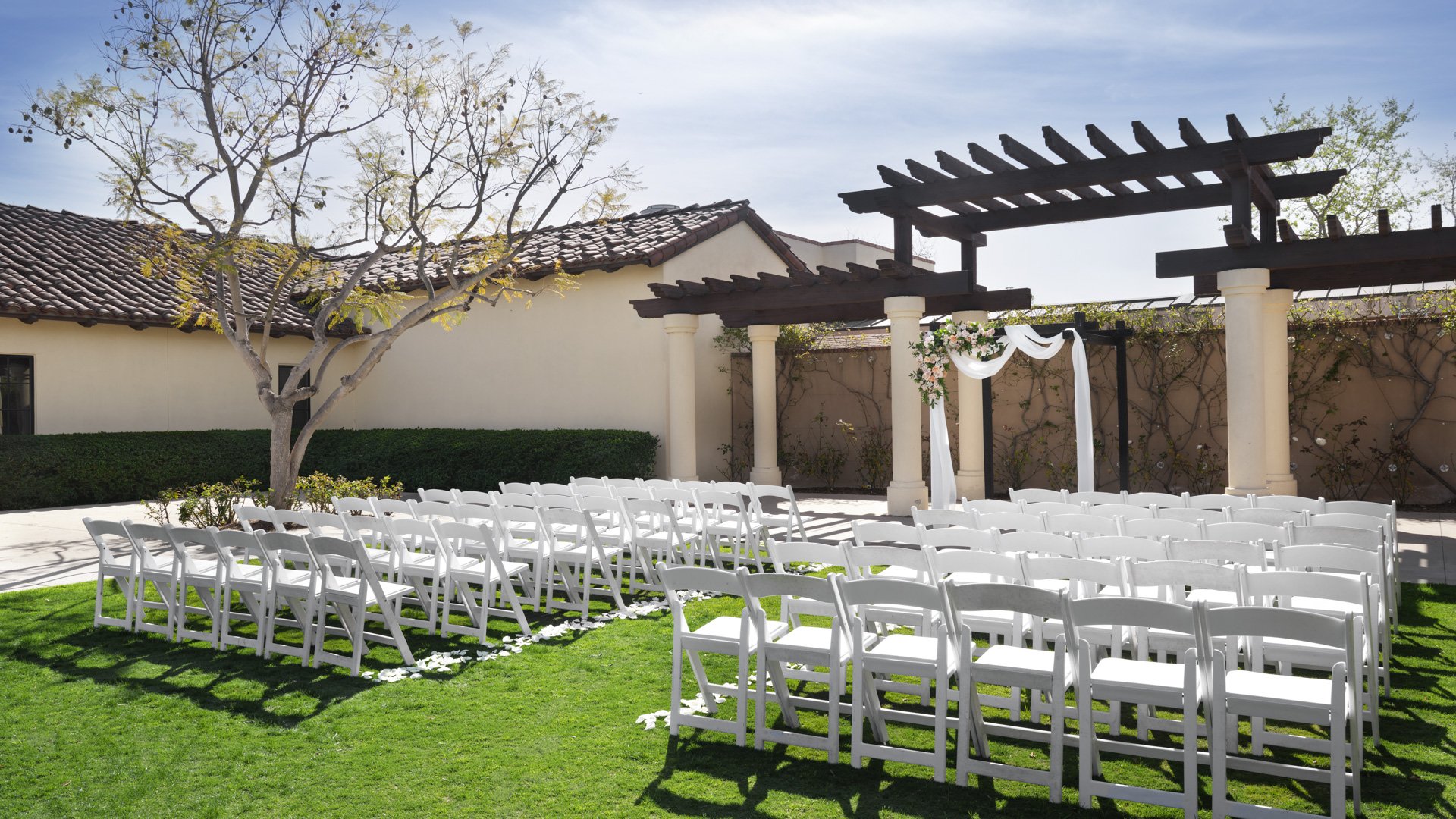 Beautiful outdoor wedding ceremony setup with white folding chairs, wooden pergola altar with floral draping, and manicured lawn at Aliso Viejo by Wedgewood Weddings venue