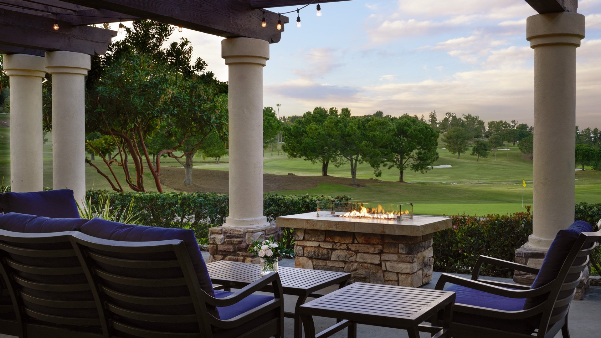 Romantic evening patio setting with modern fire table, navy seating, stone columns, and panoramic golf course views at Aliso Viejo by Wedgewood Weddings