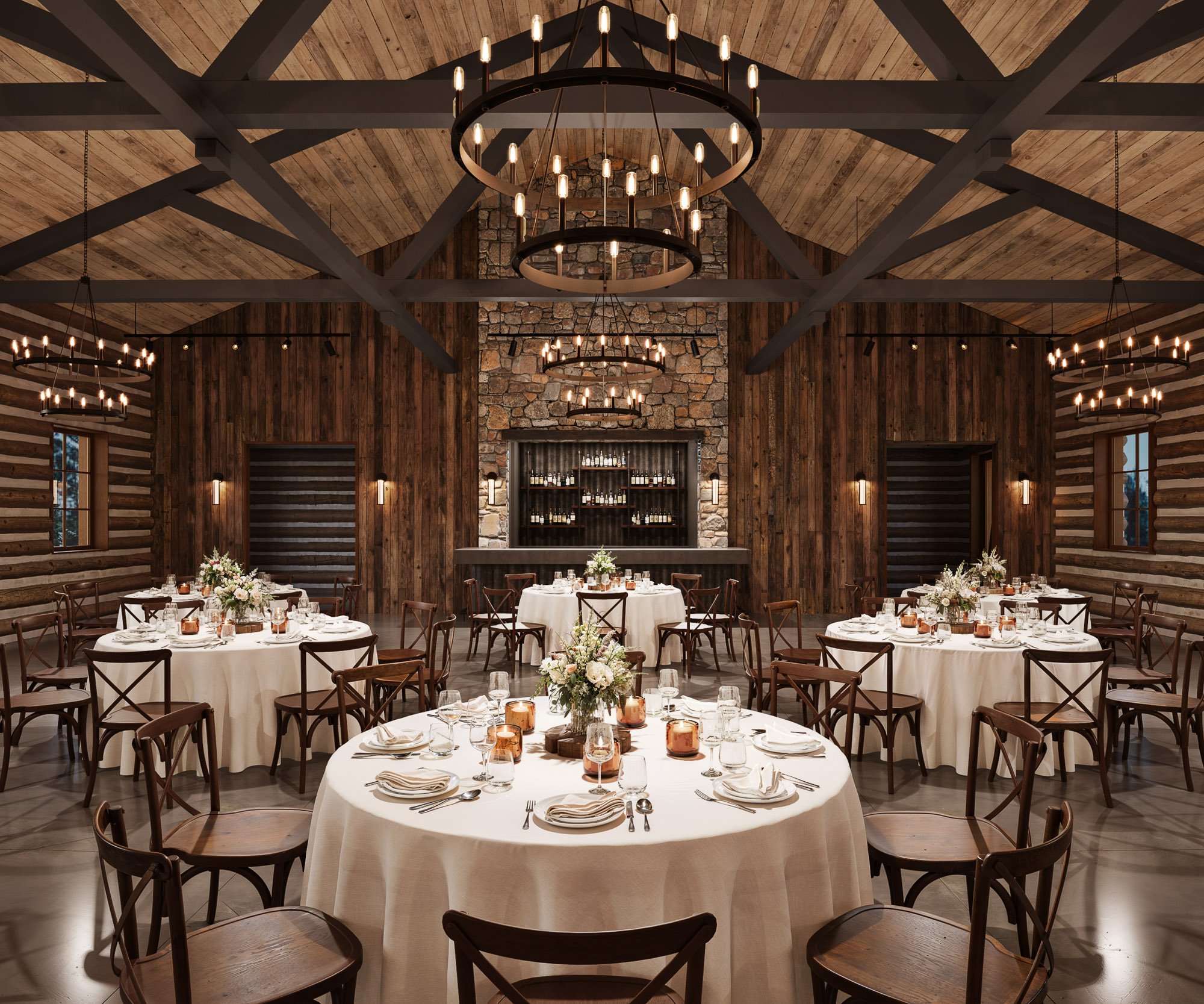 Elegant log cabin reception space at Casa del Rio with wooden walls, exposed beam ceiling, circular chandeliers, stone bar backdrop, and round dining tables with amber accents.