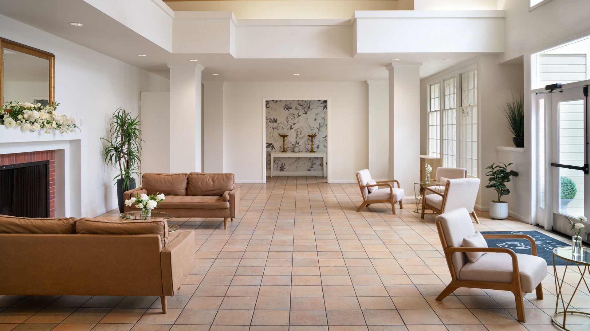 Spacious interior lobby at Cuvier Club featuring leather seating, brick fireplace, coffered ceilings, tropical plants, and elegant decor for wedding guests in La Jolla