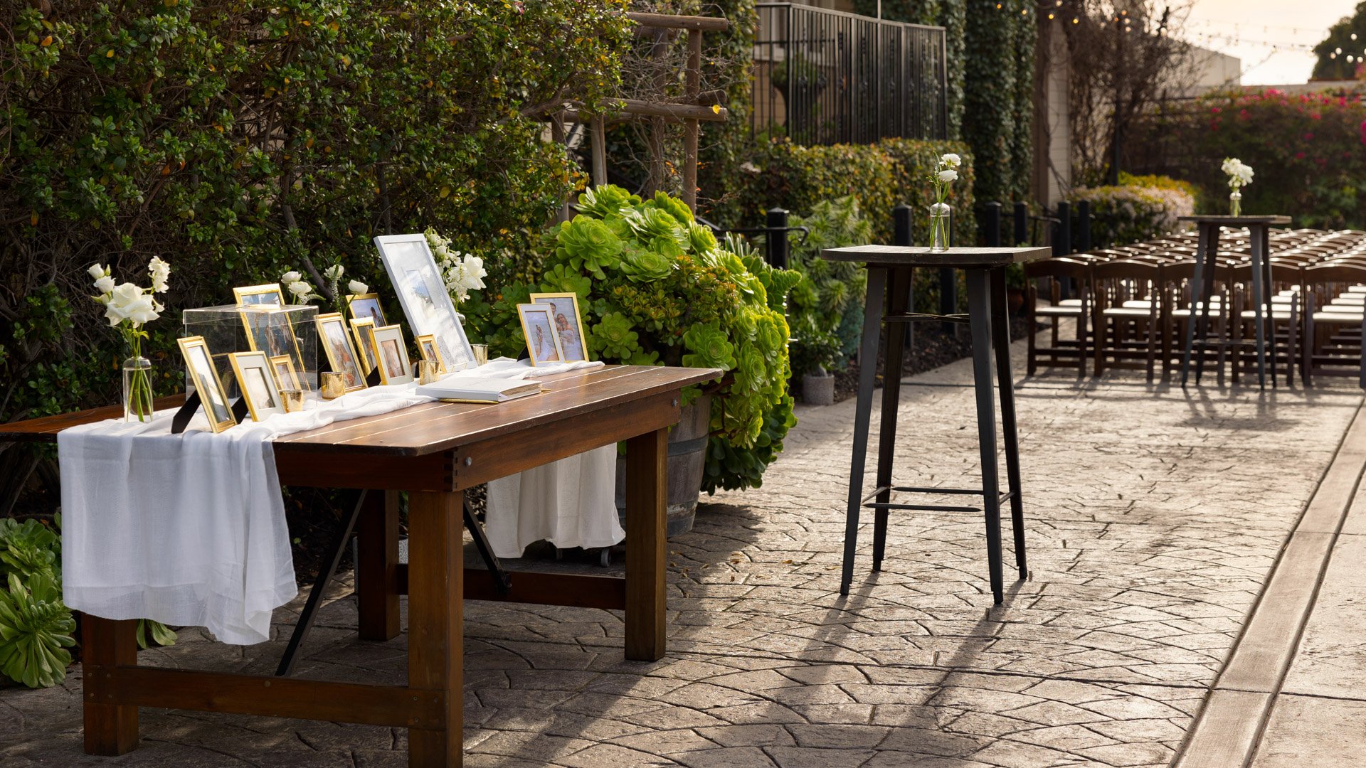 Elegant memory table display in the Garden Courtyard at Cuvier Club by Wedgewood Weddings featuring gold-framed photos, white floral arrangements, and rustic wooden table for La Jolla weddings