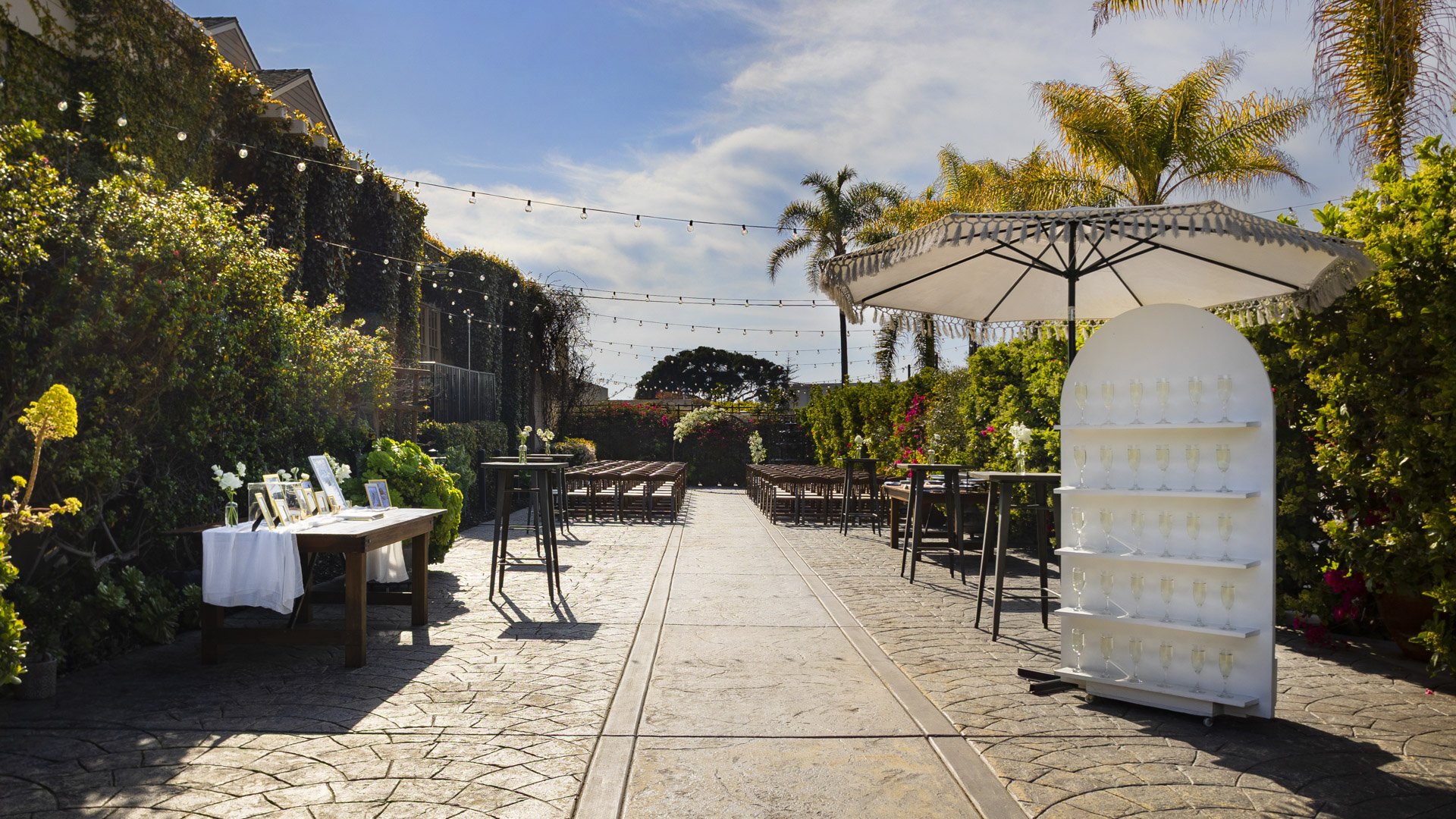 Complete Garden Courtyard wedding setup at Cuvier Club La Jolla featuring ceremony seating, elegant champagne wall, tropical landscaping, and string lights for outdoor celebrations