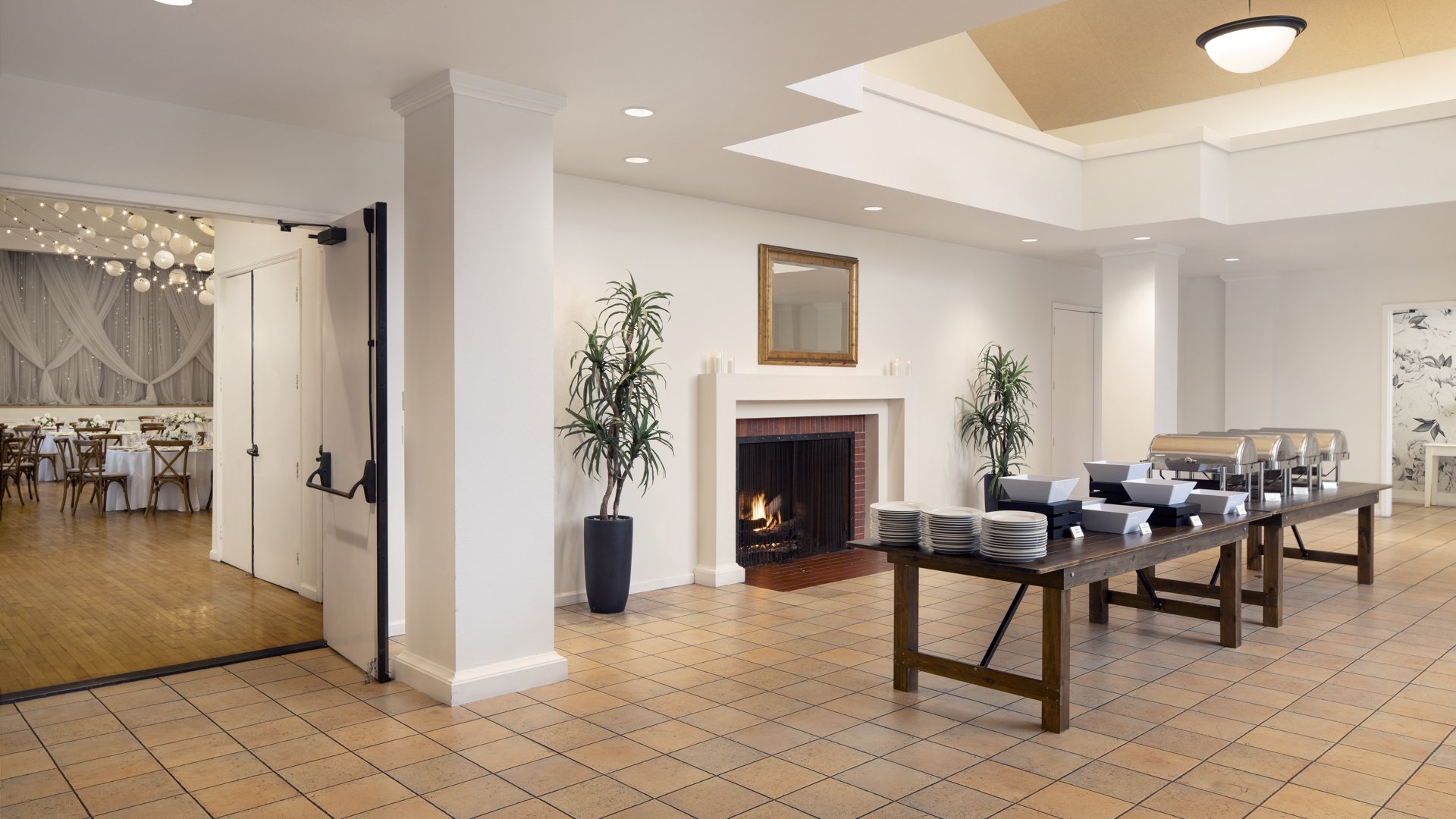 Professional wedding catering buffet setup at Cuvier Club featuring elegant serving stations, white dinnerware, brick fireplace backdrop, and reception hall access in La Jolla