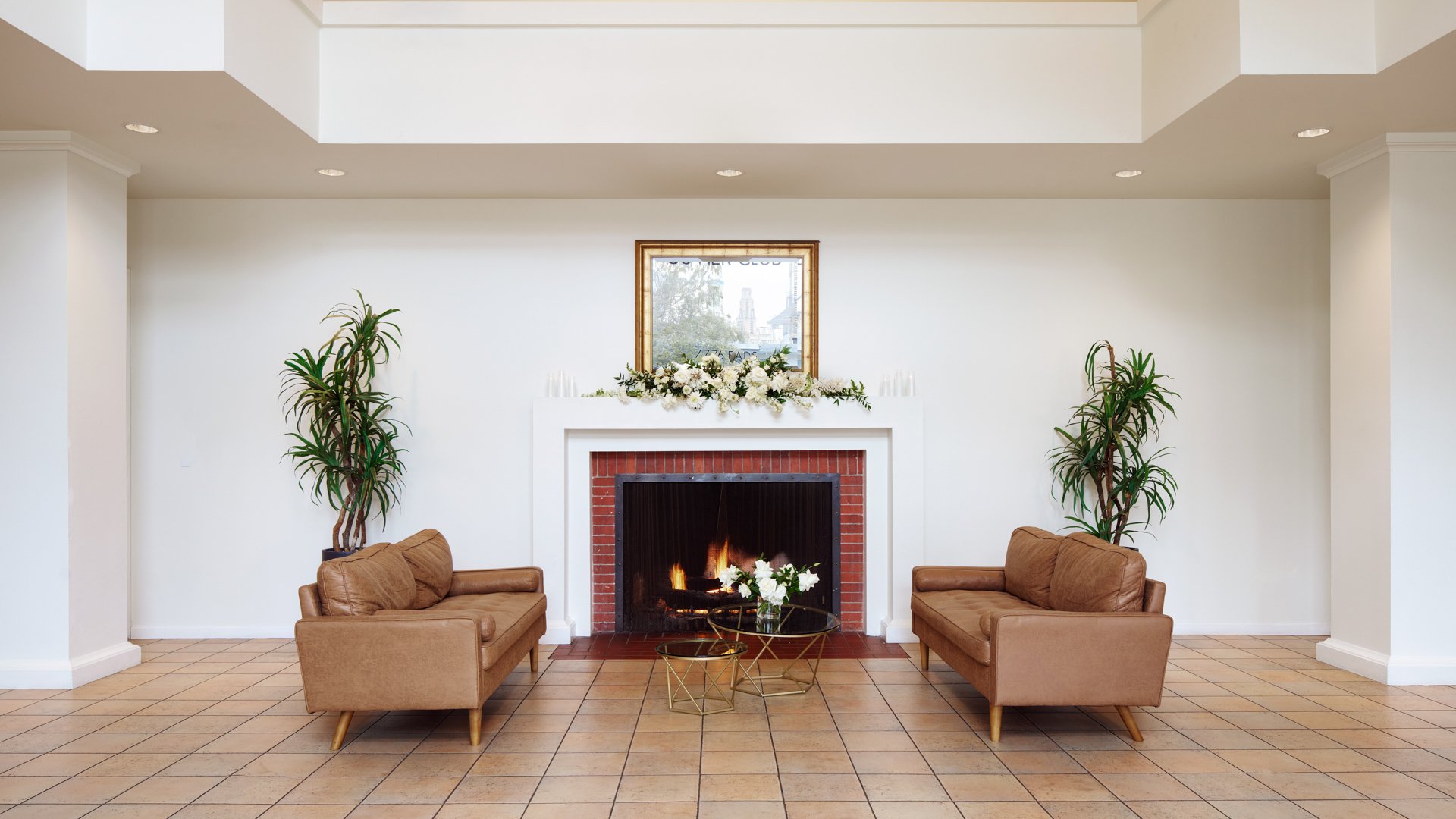 Cozy wedding reception lounge at Cuvier Club by Wedgewood Weddings featuring brick fireplace, leather armchairs, tropical plants, and intimate seating area in La Jolla