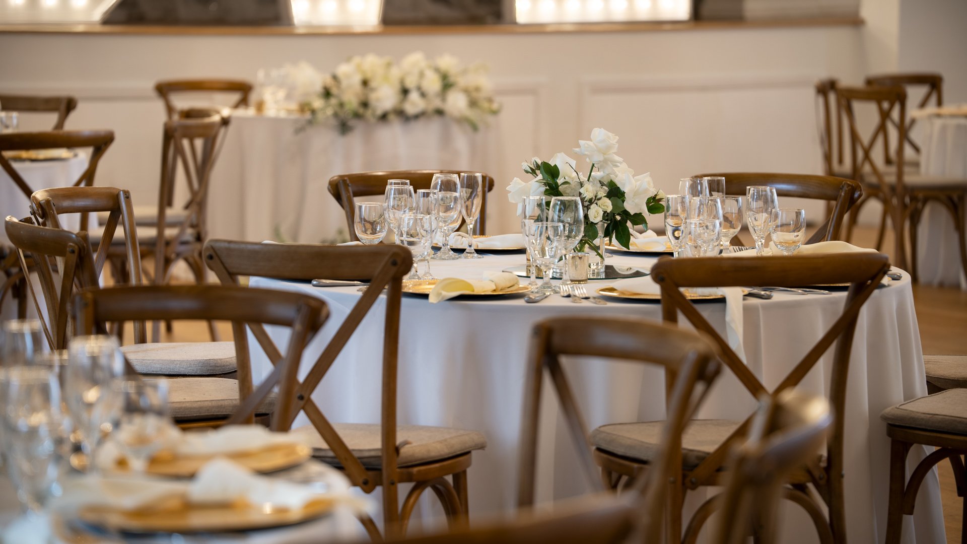Close-up of elegant wedding reception table setting at Cuvier Club featuring cross-back chairs, white floral centerpieces, crystal glassware, and gold charger plates for La Jolla weddings