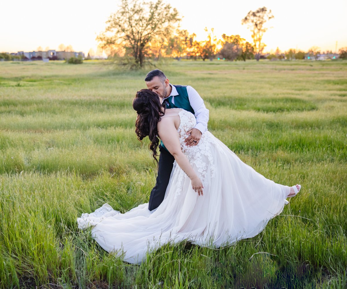 Bride and groom kissing in green grassy field at sunset - Evergreen Springs by Wedgewood Weddings - 1