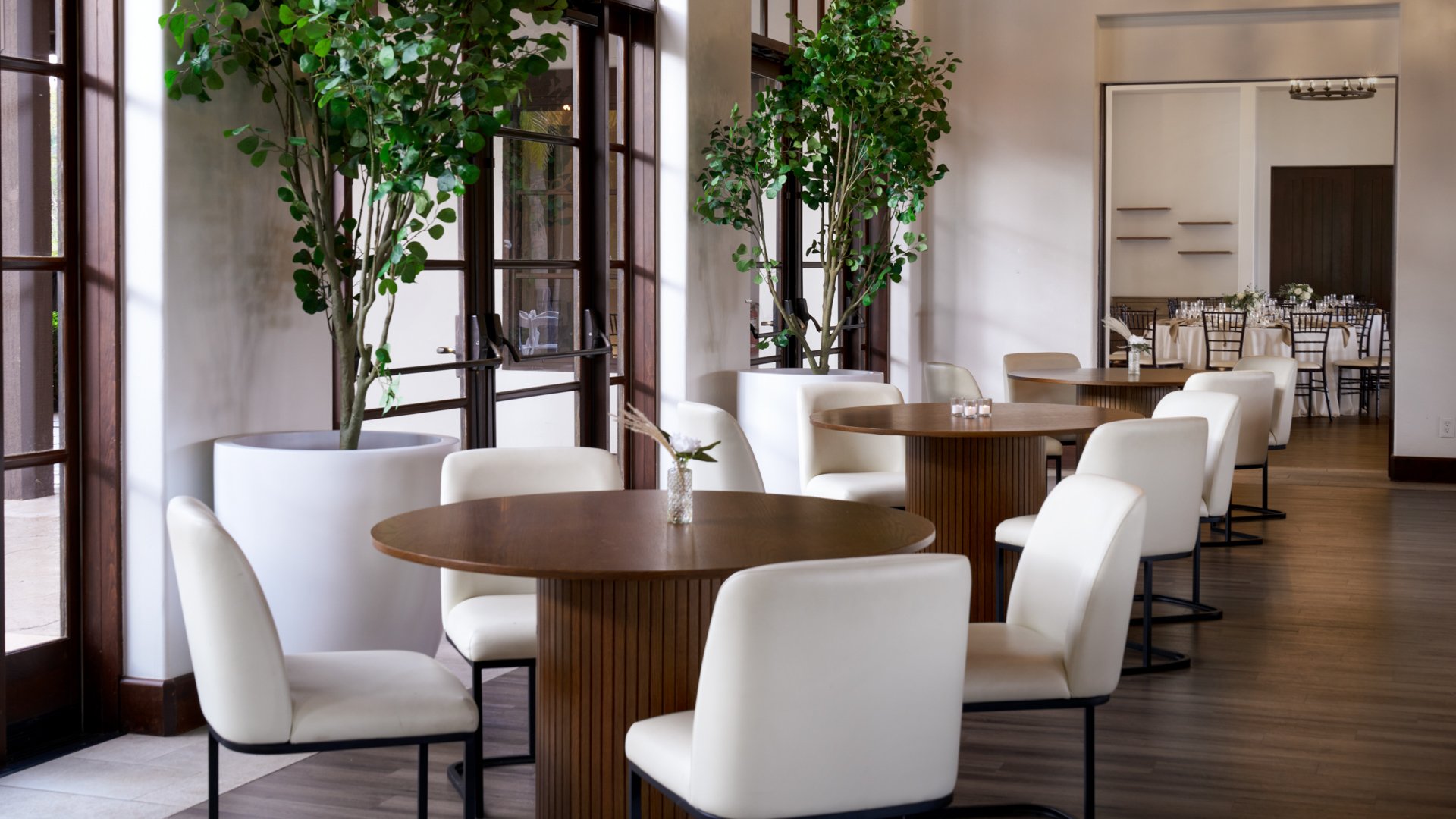 Contemporary wedding cocktail lounge at Fallbrook Estate featuring round high-top tables, cream upholstered chairs, floor-to-ceiling windows and modern interior design for intimate wedding receptions