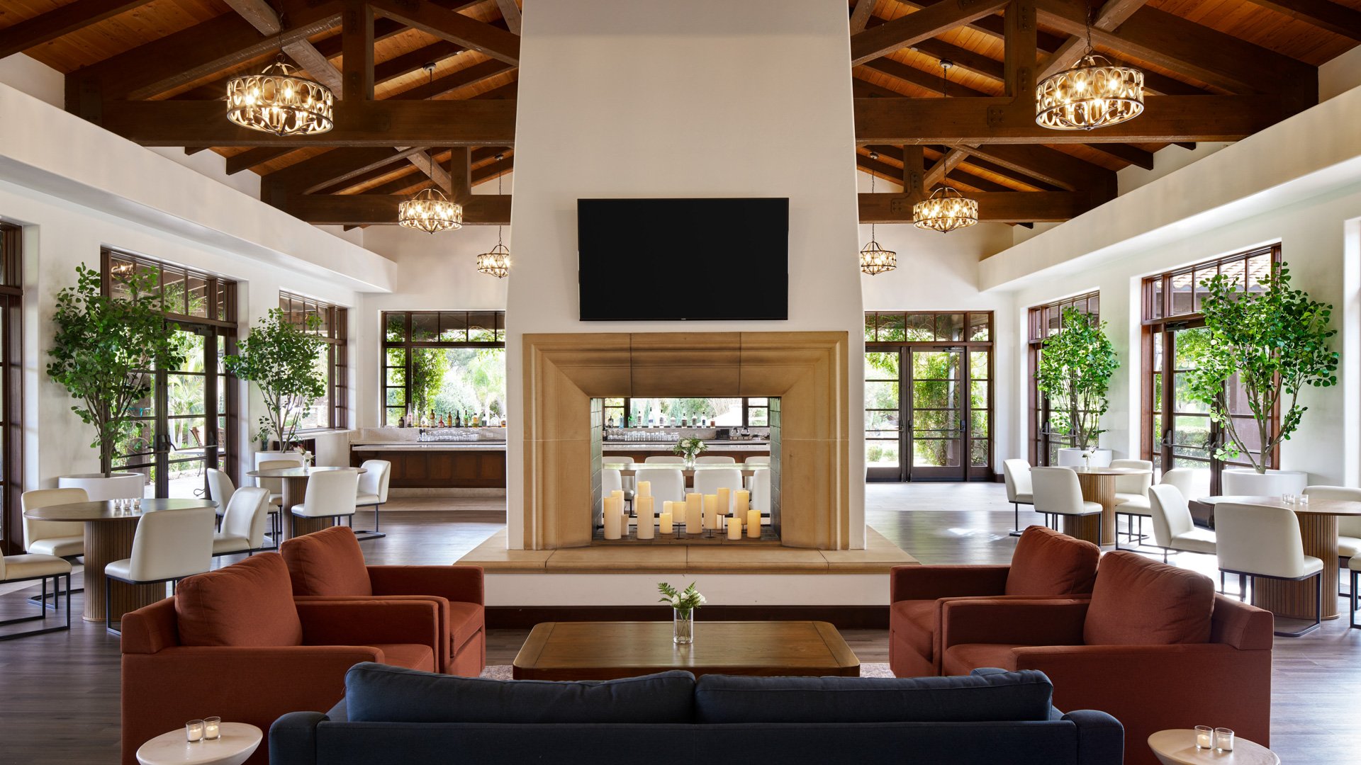 Contemporary wedding reception lounge at Fallbrook Estate featuring exposed wood beams, geometric chandeliers, modern furniture, two-way fireplace and floor-to-ceiling windows