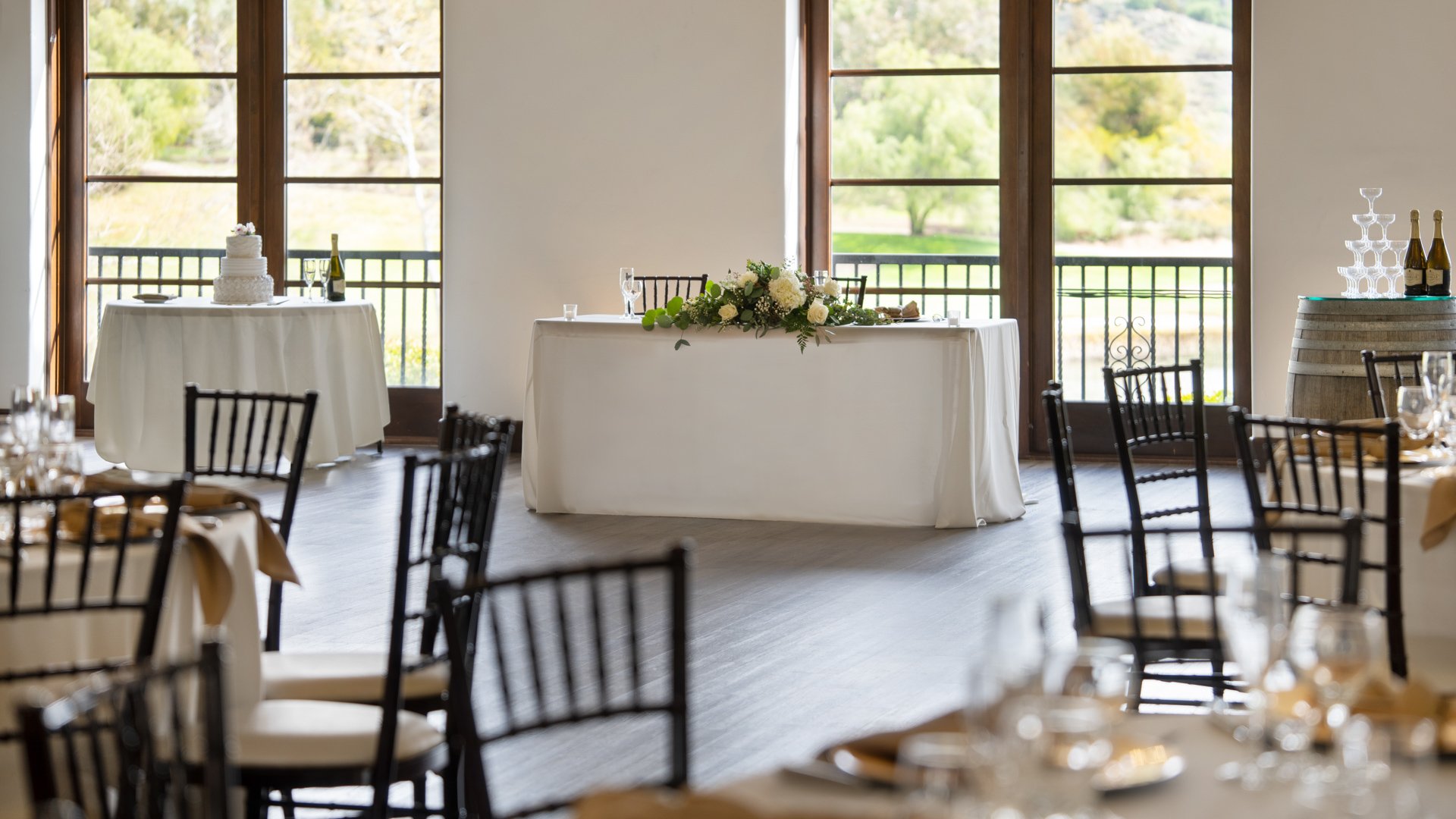Beautiful sweetheart table setup at Fallbrook Estate Wedgewood Weddings with white floral garland, Chiavari chairs, cake table and panoramic windows overlooking golf course in Fallbrook California