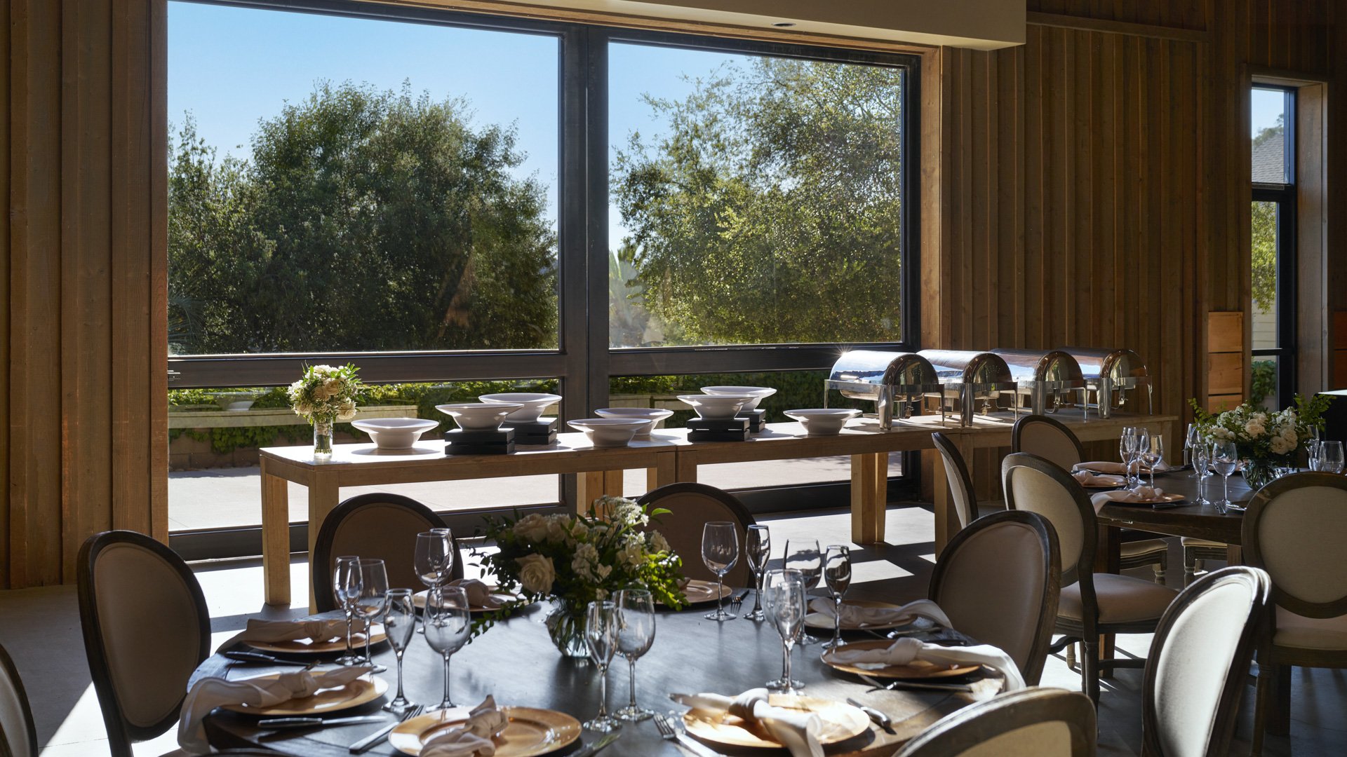 Professional catering setup at Galway Downs featuring buffet service stations, elegant serving dishes, crystal stemware, and garden views through large windows for wedding receptions in Temecula