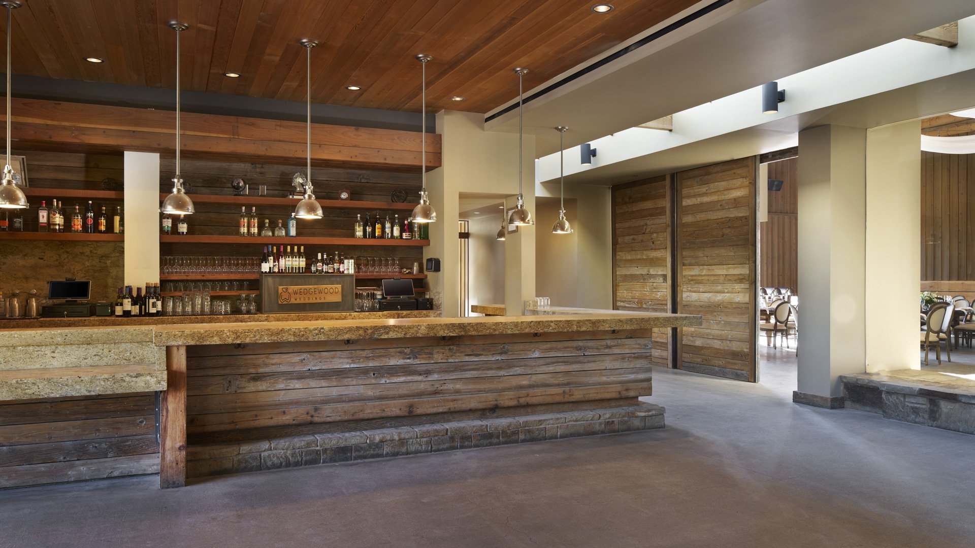 Impressive grand bar at Galway Downs featuring reclaimed wood construction, granite countertops, pendant lighting, full liquor service, and open entrance to reception hall in Temecula wine country