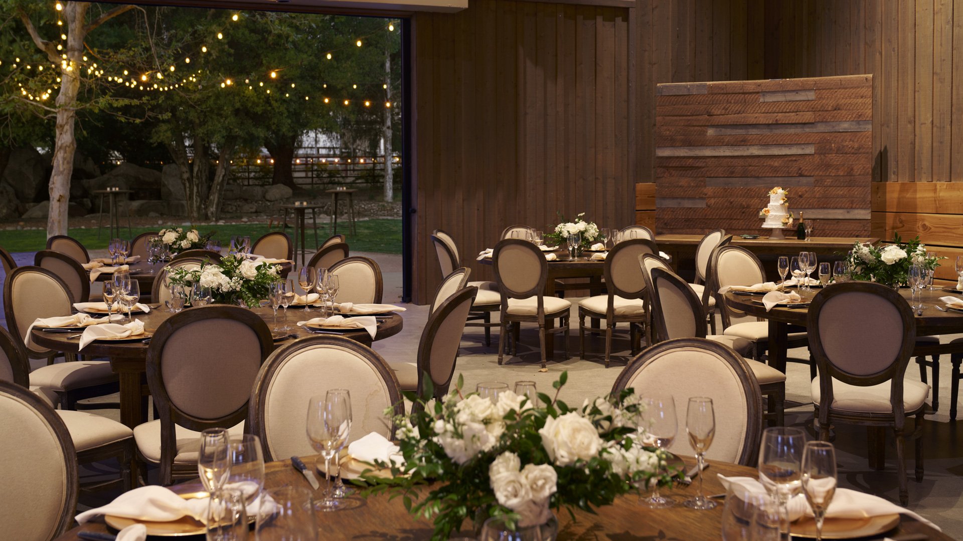 Sophisticated wedding reception at Galway Downs with round tables, neutral chair covers, white floral centerpieces, and panoramic views of manicured gardens through large windows