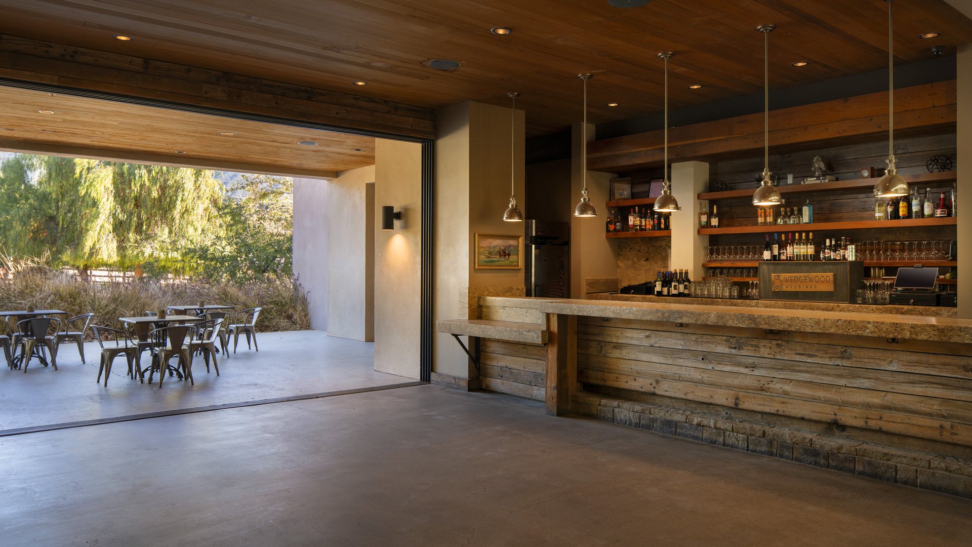 Stunning rustic bar at Galway Downs featuring reclaimed wood construction, pendant lighting, full-service bartending station, and open-air patio seating for wedding receptions in Temecula