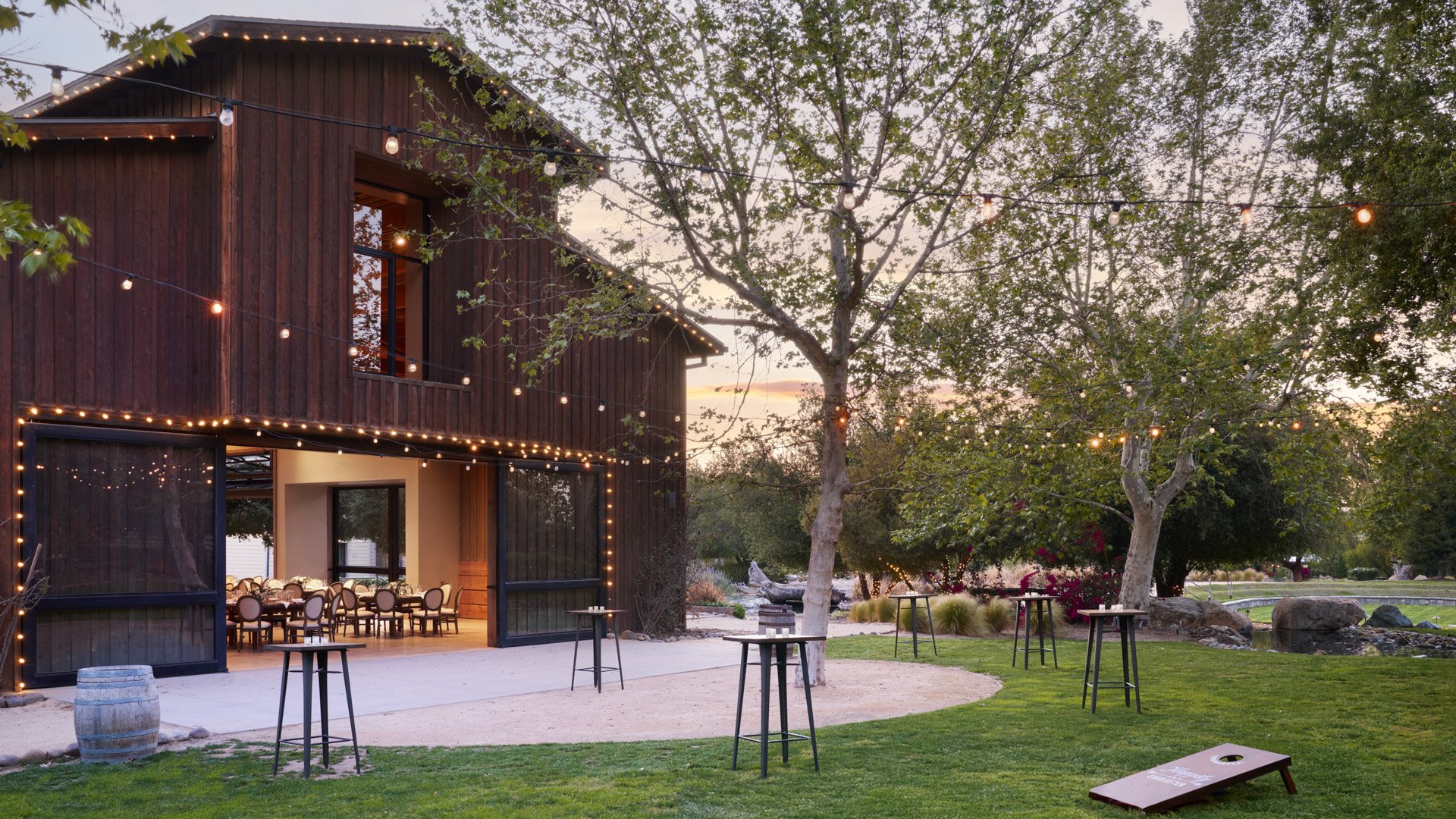 Charming rustic wedding barn at Galway Downs decorated with warm string lights and cocktail tables, perfect for outdoor evening receptions in Temecula wine country
