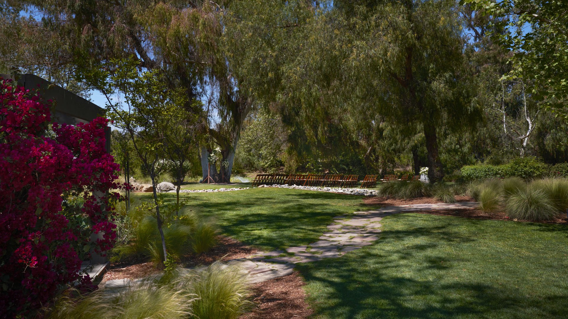 Beautiful garden wedding ceremony space at Galway Downs featuring stone pathways, lush landscaping, vibrant bougainvillea, and serene ceremony seating under ancient trees