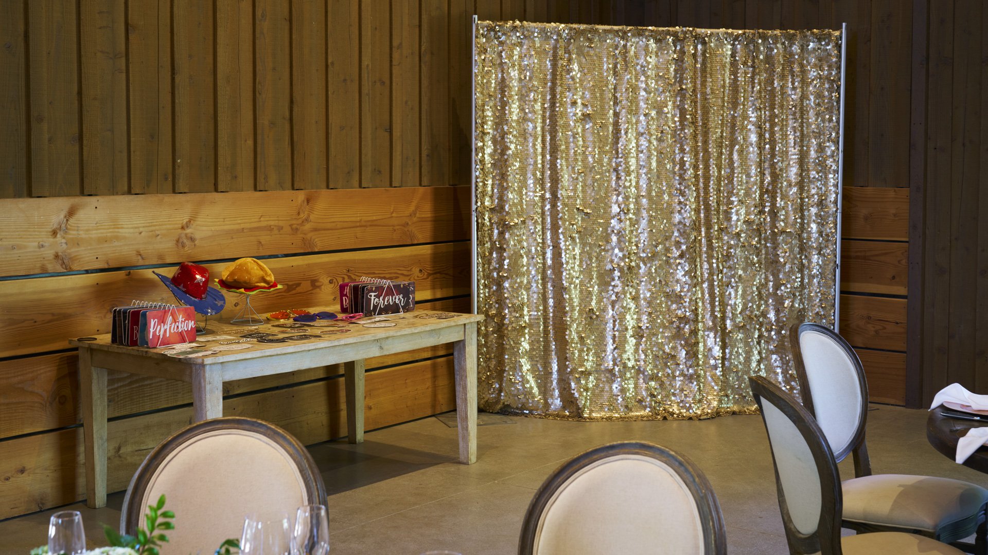 Fun wedding photo booth setup at Galway Downs featuring gold sequin backdrop, rustic wooden props table with colorful accessories, and elegant seating area for guest entertainment in Temecula, California