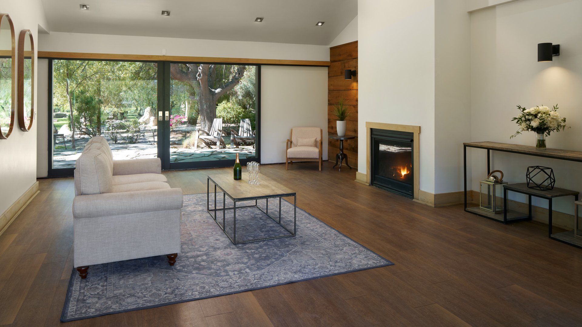 Sophisticated lounge area in Galway Downs Wedding Suites featuring modern fireplace, comfortable seating, floor-to-ceiling windows, and garden views for wedding party relaxation in Temecula, California