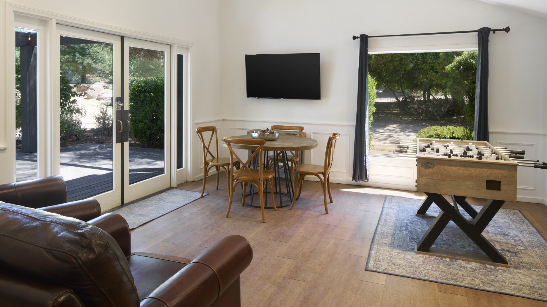 Comfortable lounge area in Galway Downs Wedding Suites with leather seating, rustic dining table, entertainment center, and patio access for wedding party relaxation in Temecula
