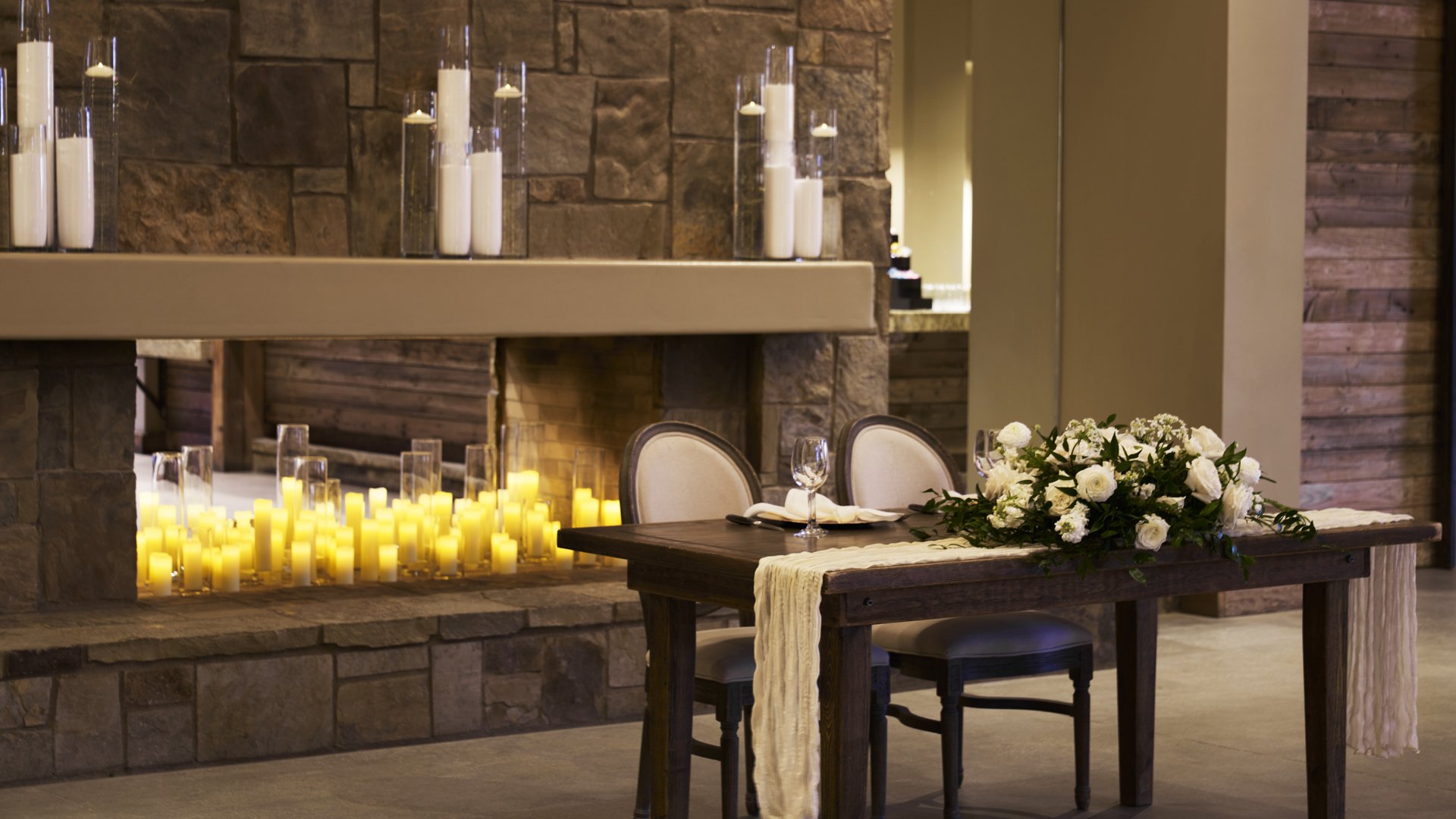 Intimate sweetheart table setup in Galway Downs Wedding Suites featuring a grand stone fireplace, romantic candle displays, and elegant floral arrangements for bride and groom dining