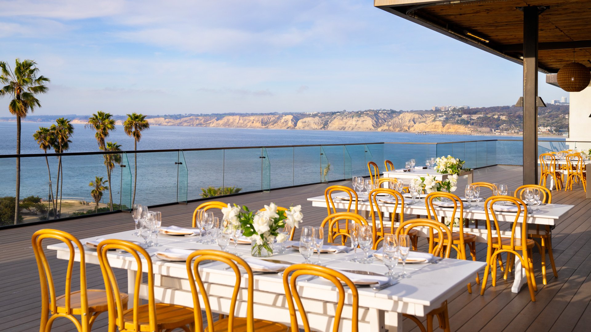 Bright outdoor wedding reception featuring bentwood chairs, white florals, and stunning La Jolla coastline views at Cove Rooftop by Wedgewood Weddings