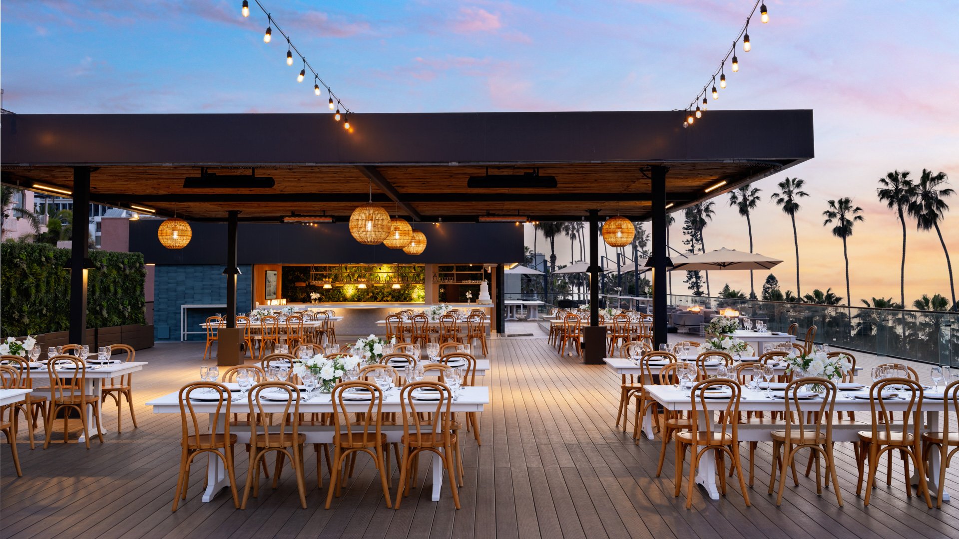 Romantic evening wedding reception setup with string lights, bentwood chairs, and oceanfront dining at La Jolla Cove Rooftop by Wedgewood Weddings