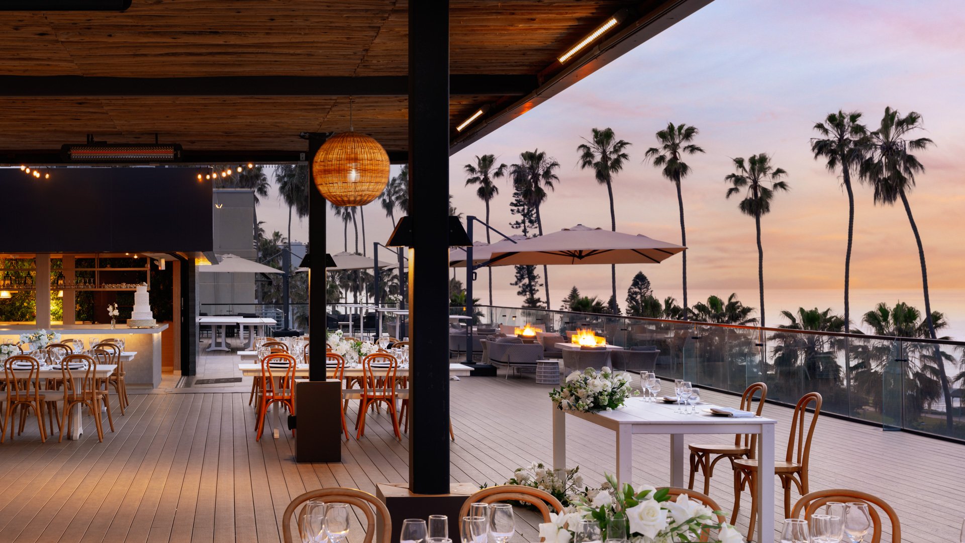 Romantic golden hour wedding reception with string lights, natural wood ceiling, and coastal sunset views at La Jolla Cove Rooftop