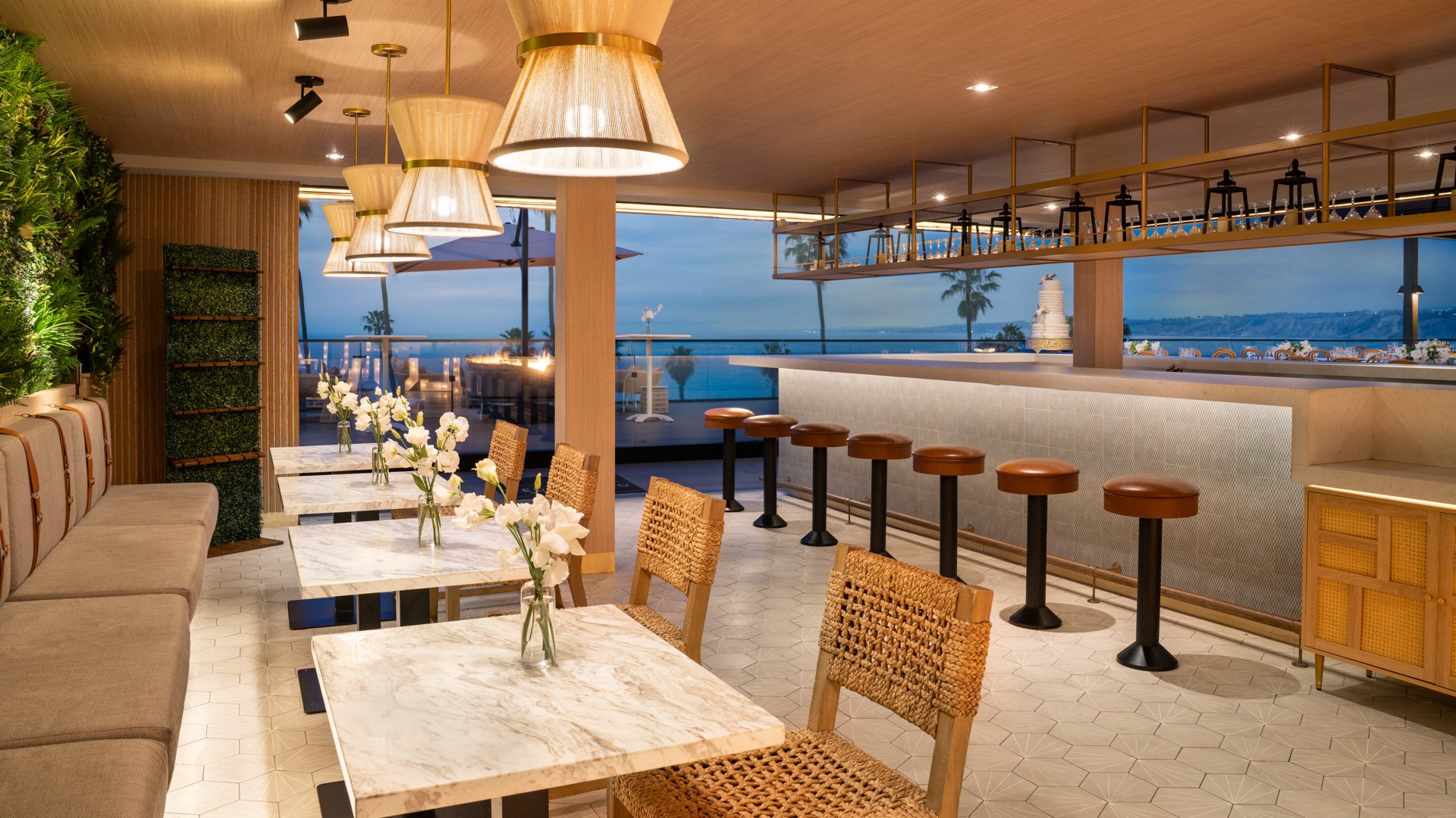 Modern indoor wedding reception space with marble tables, woven chairs, and panoramic ocean views at La Jolla Cove Rooftop wedding venue