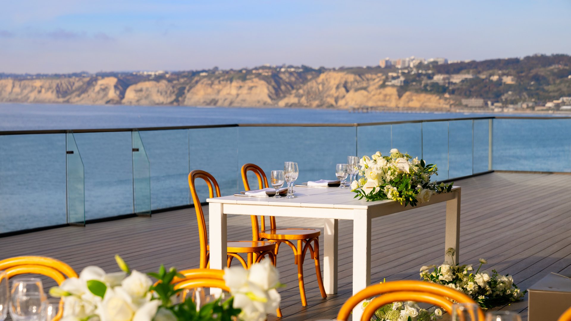Small intimate wedding reception setup with bentwood chairs, white linens, and dramatic Pacific Ocean cliff views at La Jolla Cove Rooftop