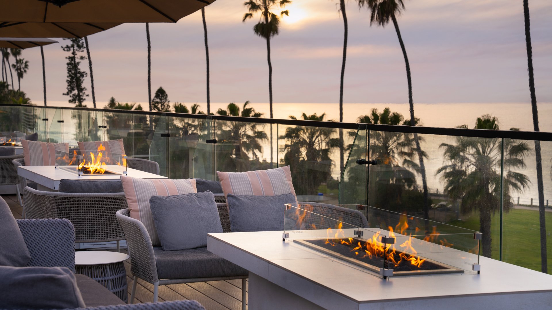 Upscale wedding cocktail hour featuring modern fire pit tables, wicker lounge seating, and panoramic Pacific Ocean views at La Jolla Cove Rooftop