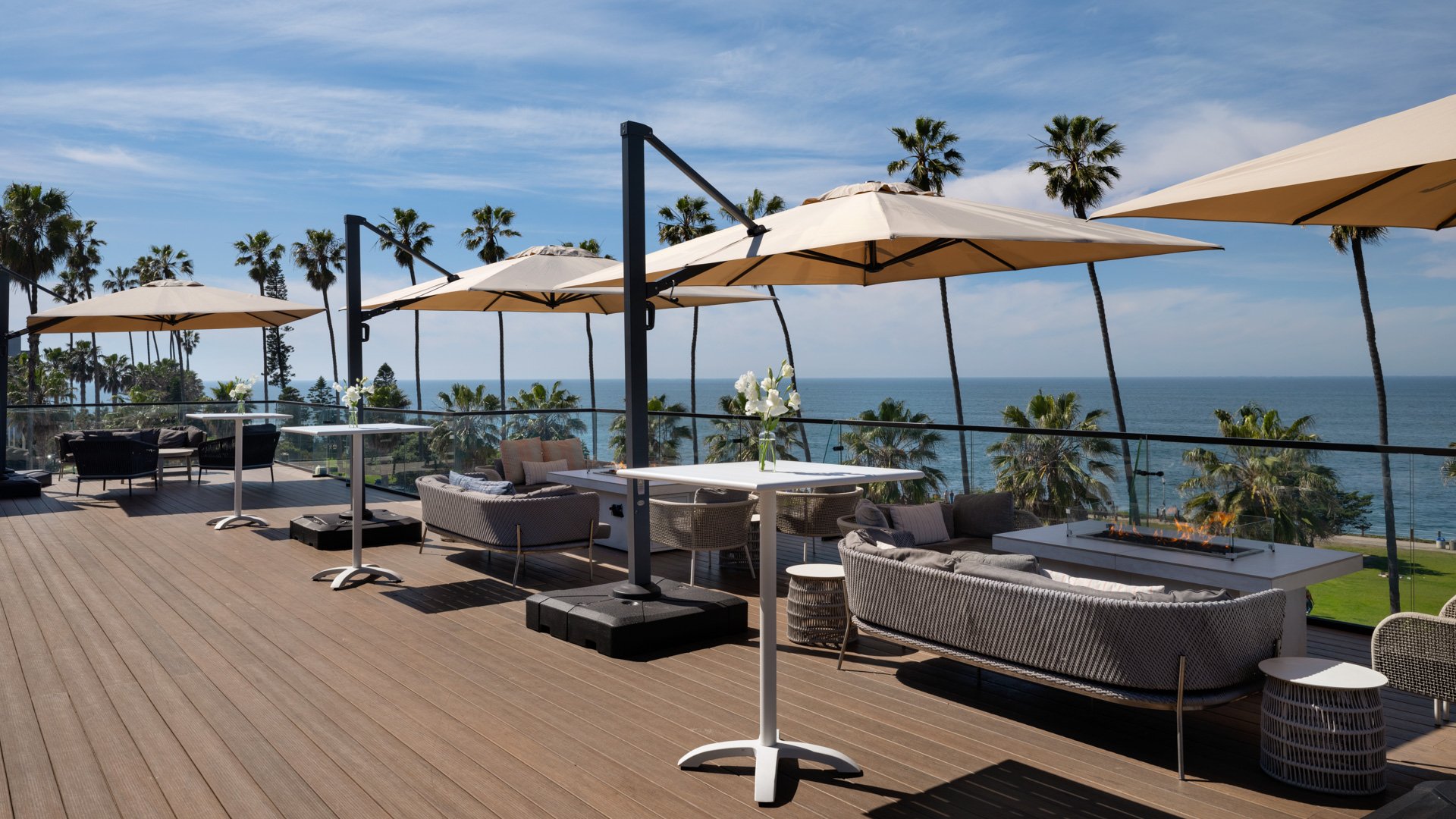 Upscale wedding cocktail lounge featuring modern wicker seating, white umbrellas, and panoramic Pacific Ocean views at La Jolla Cove Rooftop venue