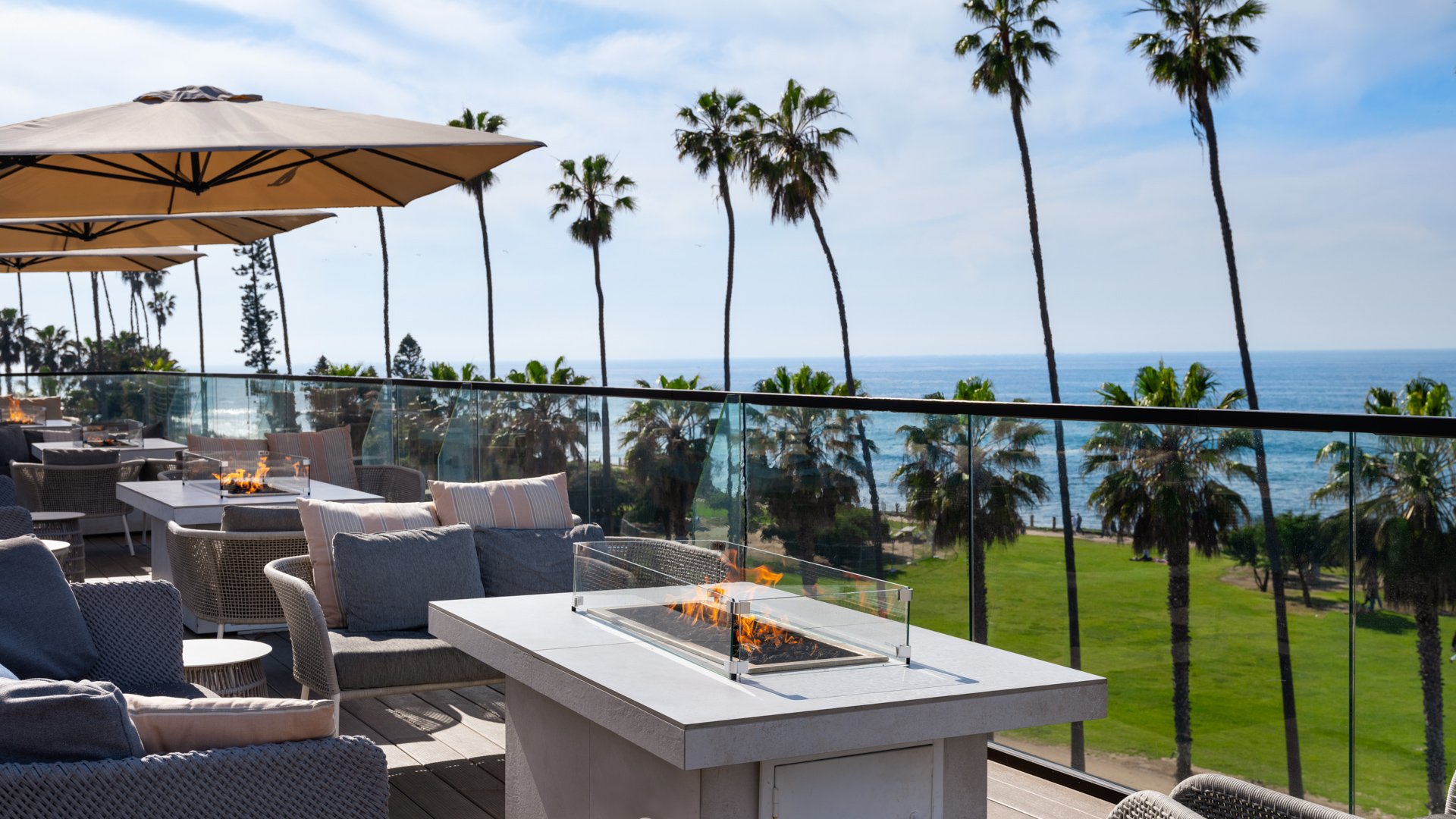Contemporary wedding lounge space with linear fire pit, wicker seating, striped pillows, and Pacific Ocean panorama at La Jolla Cove Rooftop venue
