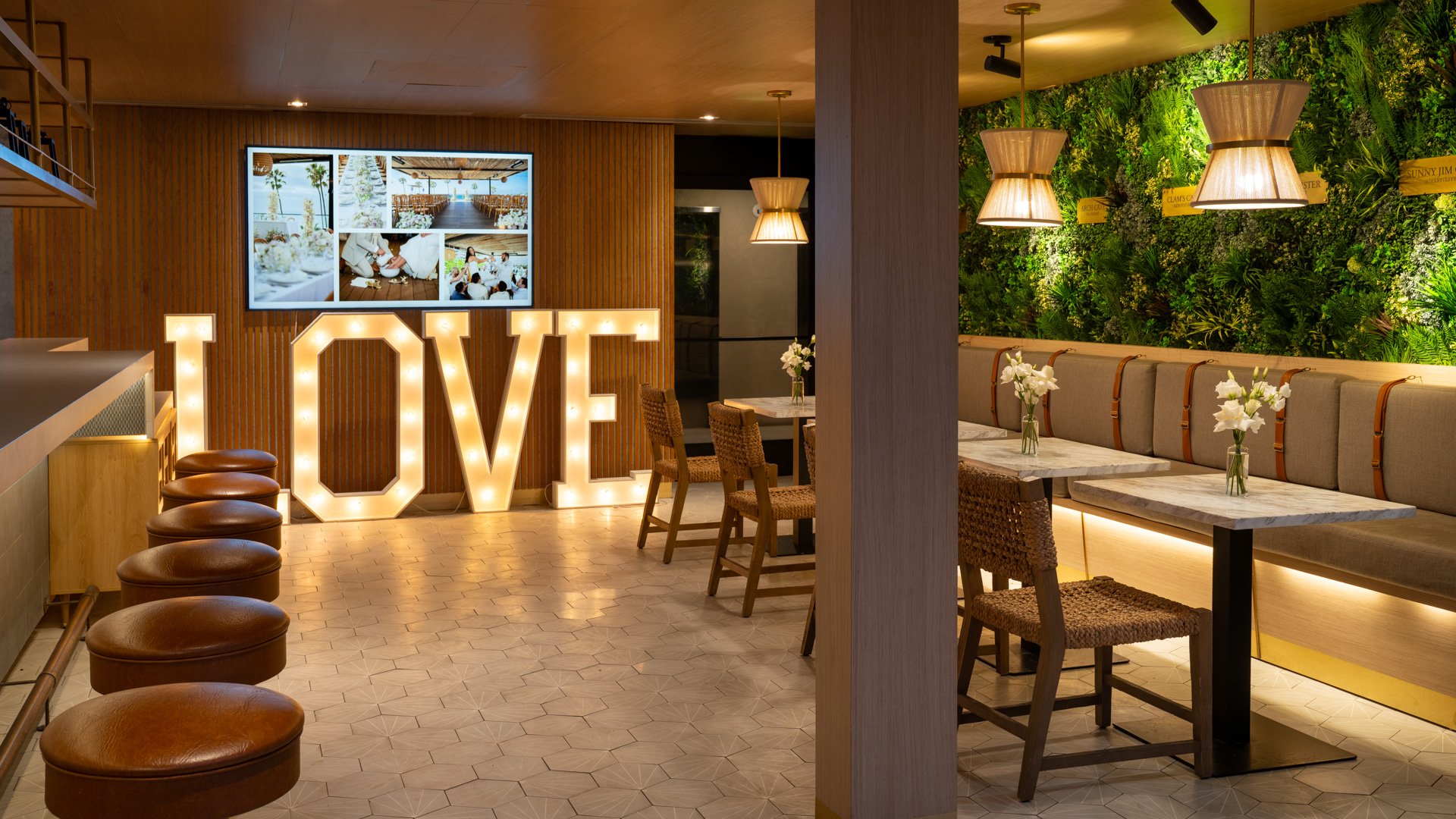 Contemporary wedding reception lounge featuring illuminated LOVE marquee letters, living wall, leather seating, and woven pendant lights at La Jolla Cove Rooftop venue by Wedgewood Weddings