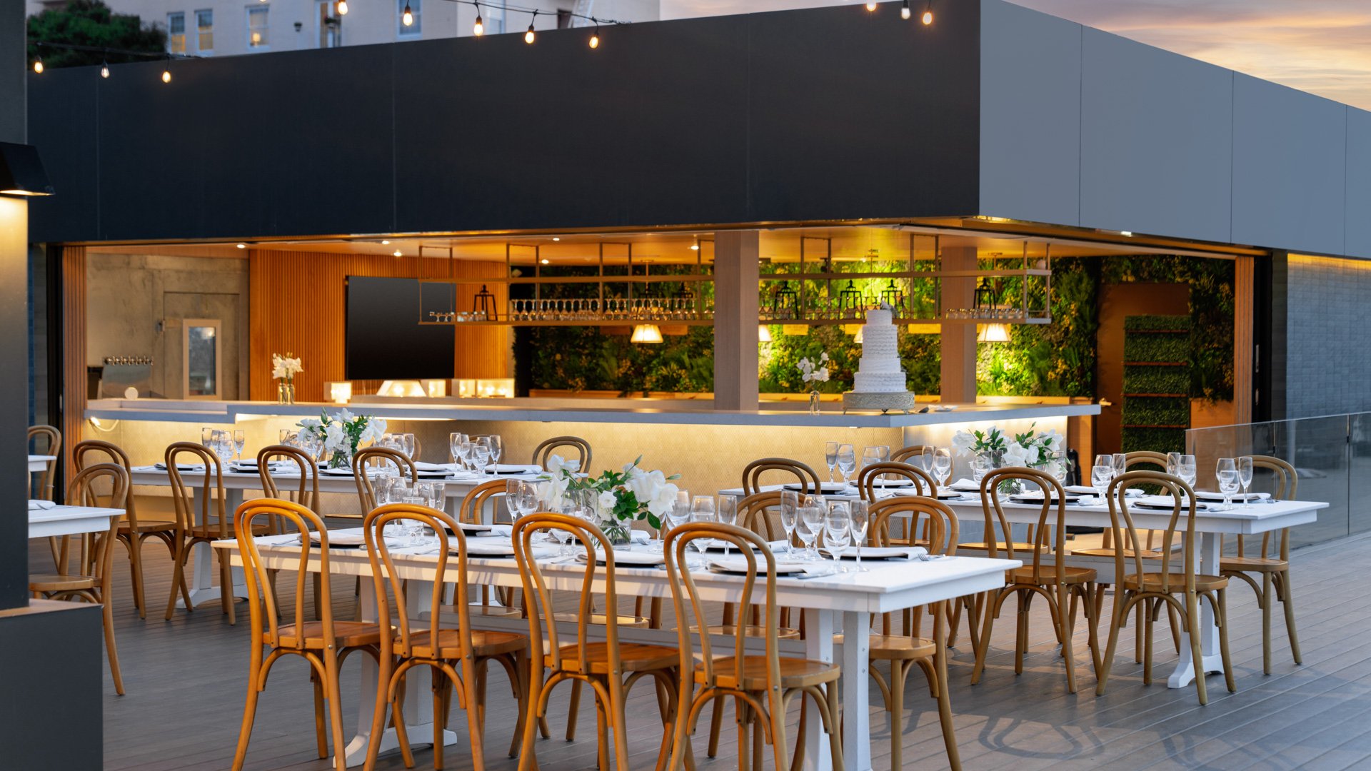 Contemporary indoor wedding reception with illuminated bar, bentwood chairs, and floor-to-ceiling ocean views at La Jolla Cove Rooftop by Wedgewood Weddings