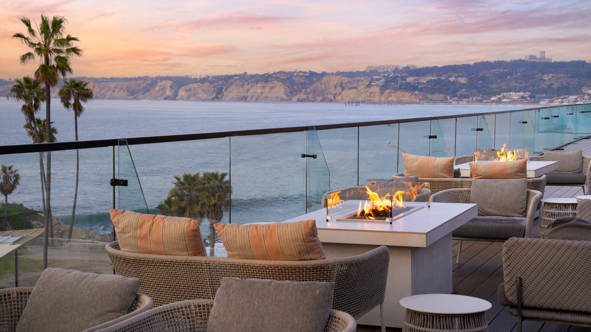 Luxury outdoor lounge area with fire pit, wicker seating, and ocean sunset views at La Jolla Cove Rooftop wedding venue in California