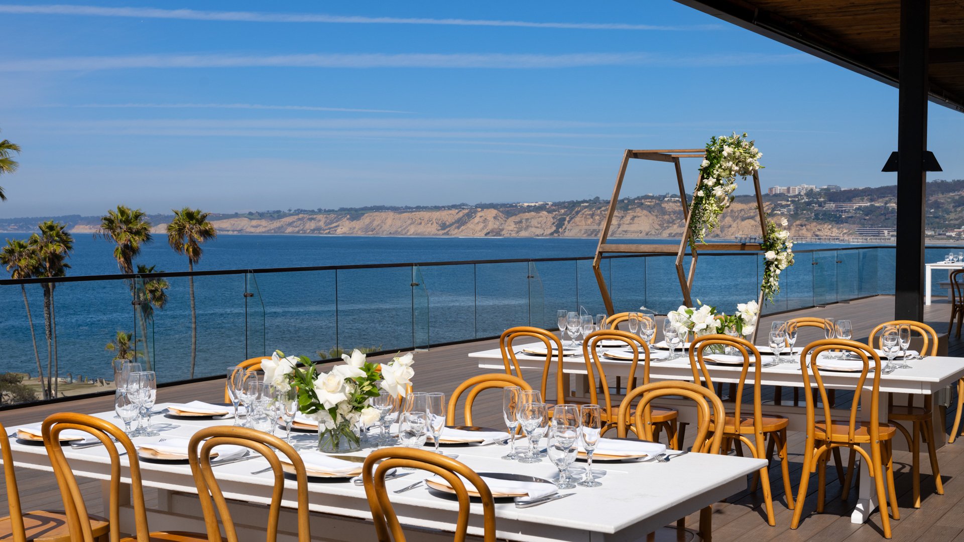 Beautiful wedding reception dining with bentwood chairs, white florals, and stunning La Jolla cliffs and Pacific Ocean views at Cove Rooftop by Wedgewood Weddings