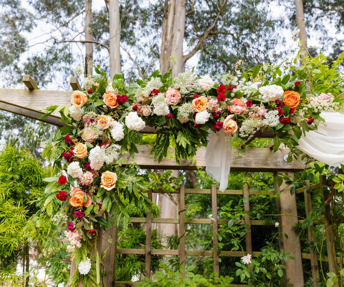 Ceremony arbor with vibrant flowers in peach, orange, and pink - Presidio Chapel at the Golden Gate Club - Wedgewood Weddings