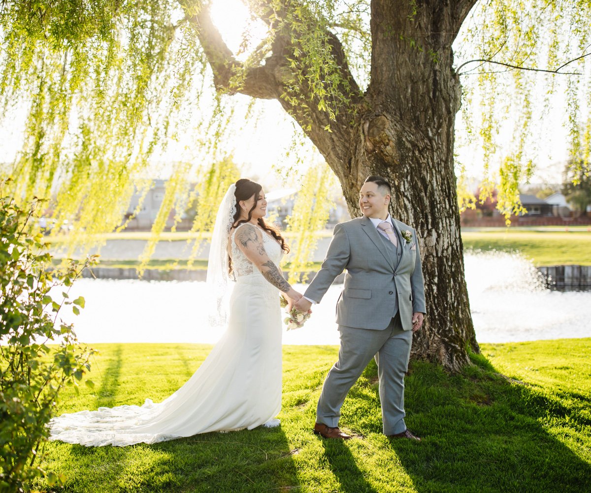 Bride and bride strolling under willow trees in front of waterfront - LGBTQ wedding - San Ramon Waters by Wedgewood Weddings