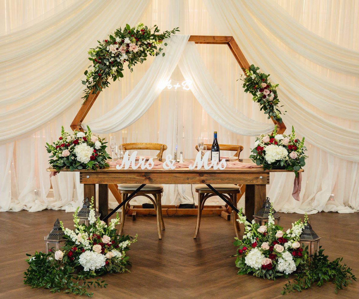 Mrs and Mrs sweetheart table with elegant drapery and pink, white, and red florals - LGBTQ wedding - San Ramon Waters by Wedgewood Weddings