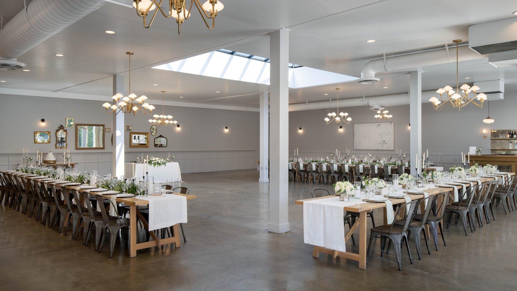 Multiple indoor dining setups with long tables, industrial chairs, and fresh floral centerpieces