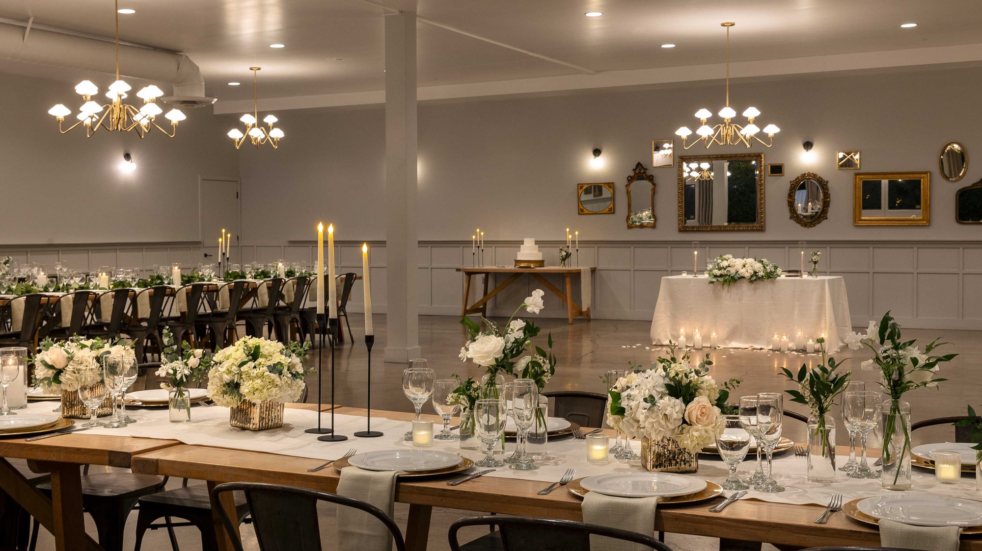 Multiple indoor dining setups with long tables, industrial chairs, and fresh floral centerpieces