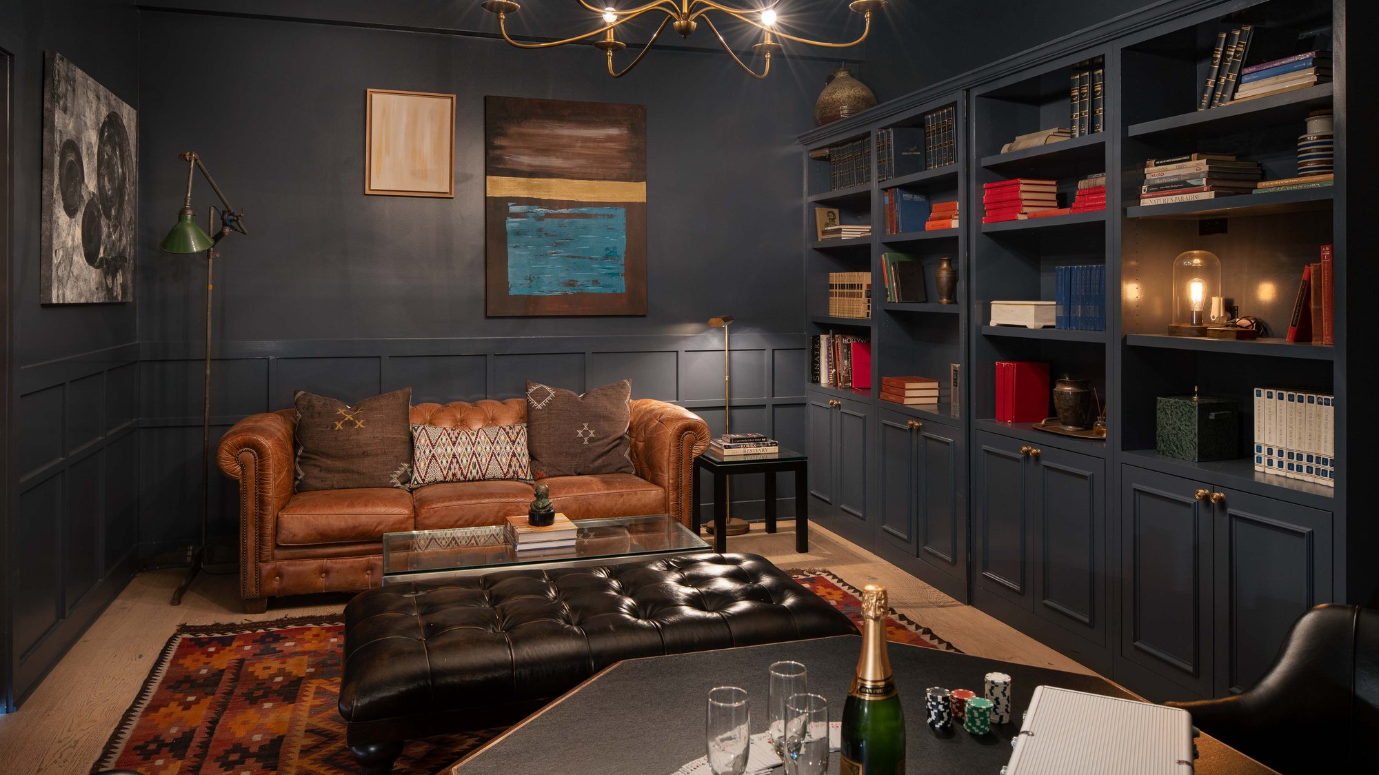 A cozy library/lounge space with dark walls, leather furniture, and bookshelves